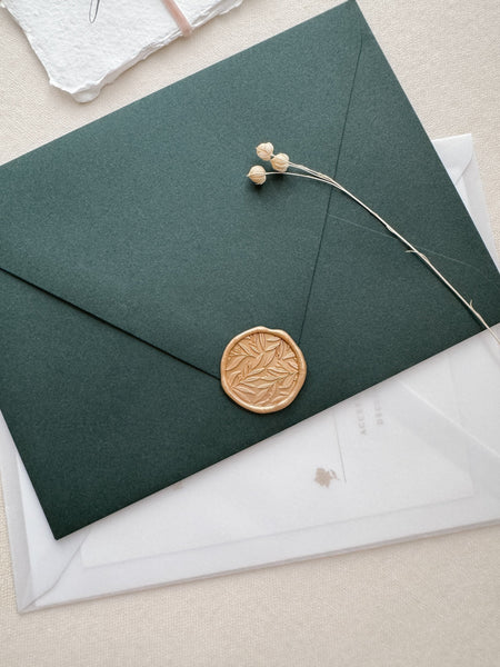 Leaf pattern light gold colored wax seal on a dark green envelope