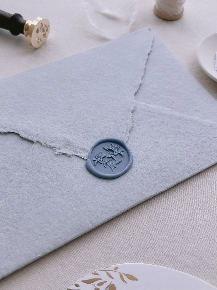 Dusty blue 3D lilies wax seal on a light blue deckle-edged handmade paper envelope