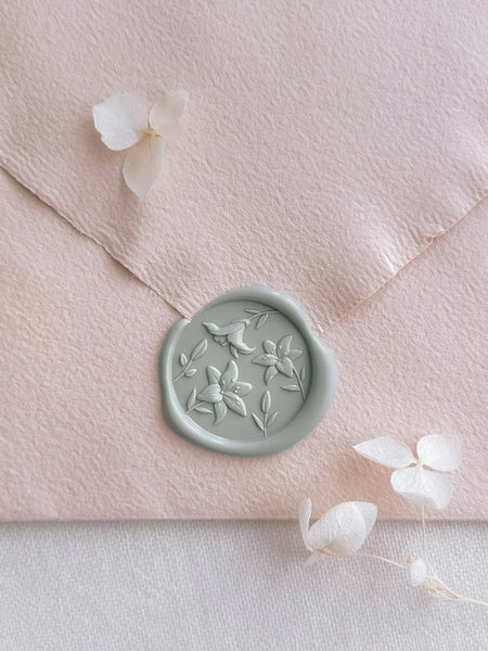 Light pastel green wax seal featuring a design of blooming lily flowers, placed on a light orange envelope