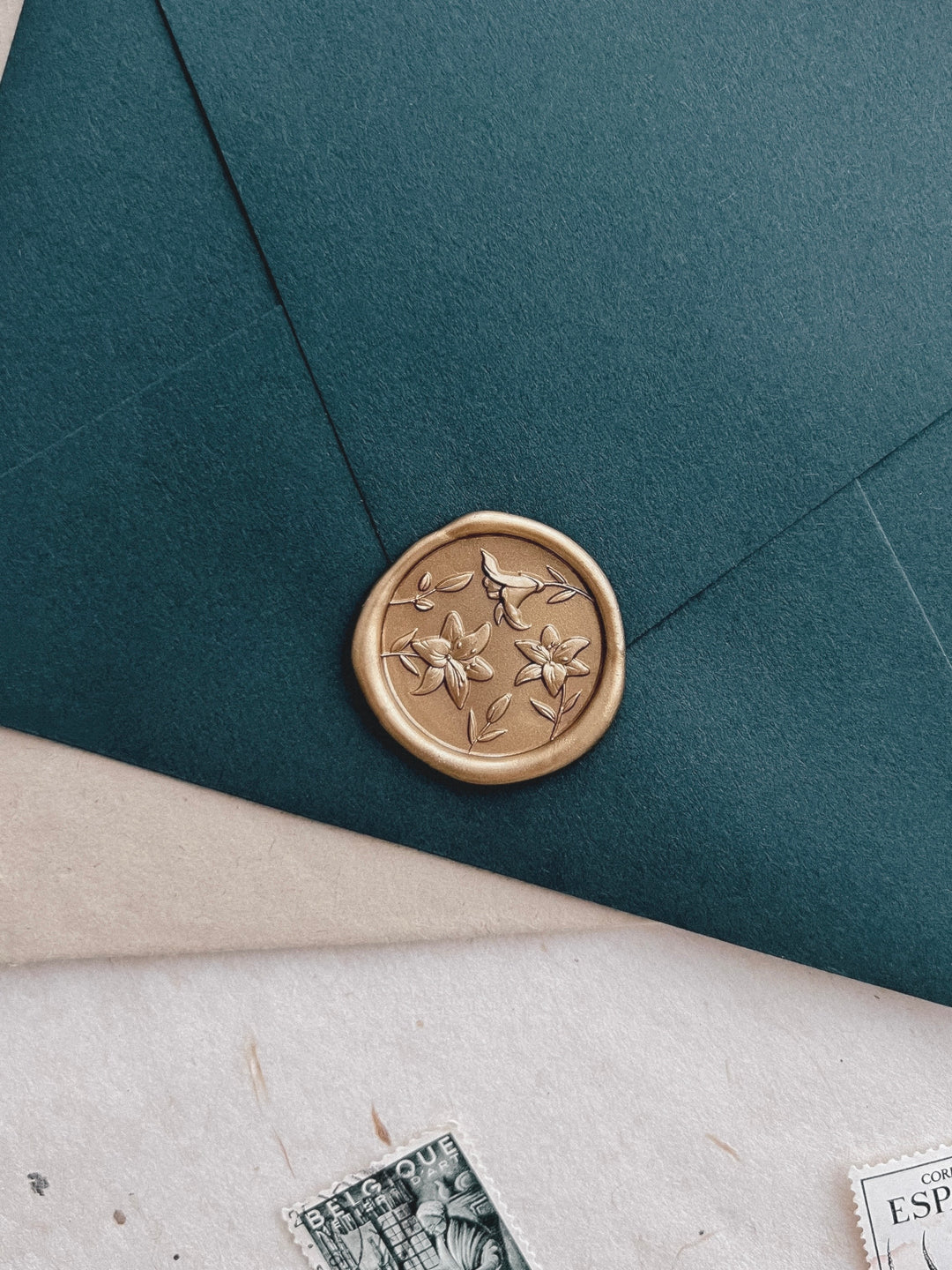 gold 3D lily blossom wax seal on a dark green envelope