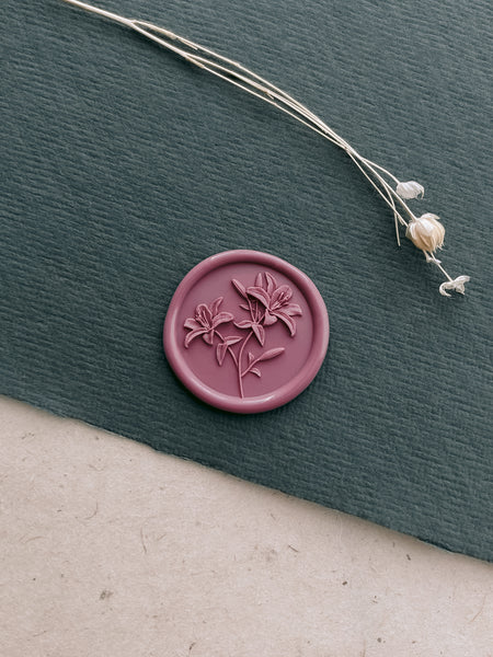 Mauve wax seal with lily flowers design on a textured green surface with dried flowers