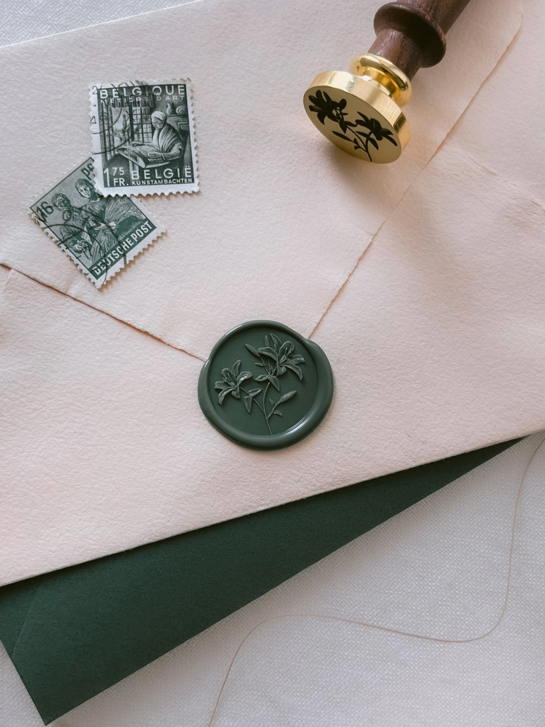 Dark green 3D lily flowers wax seal on a cream envelope next to a lilies wax stamp head with a dark brown handle