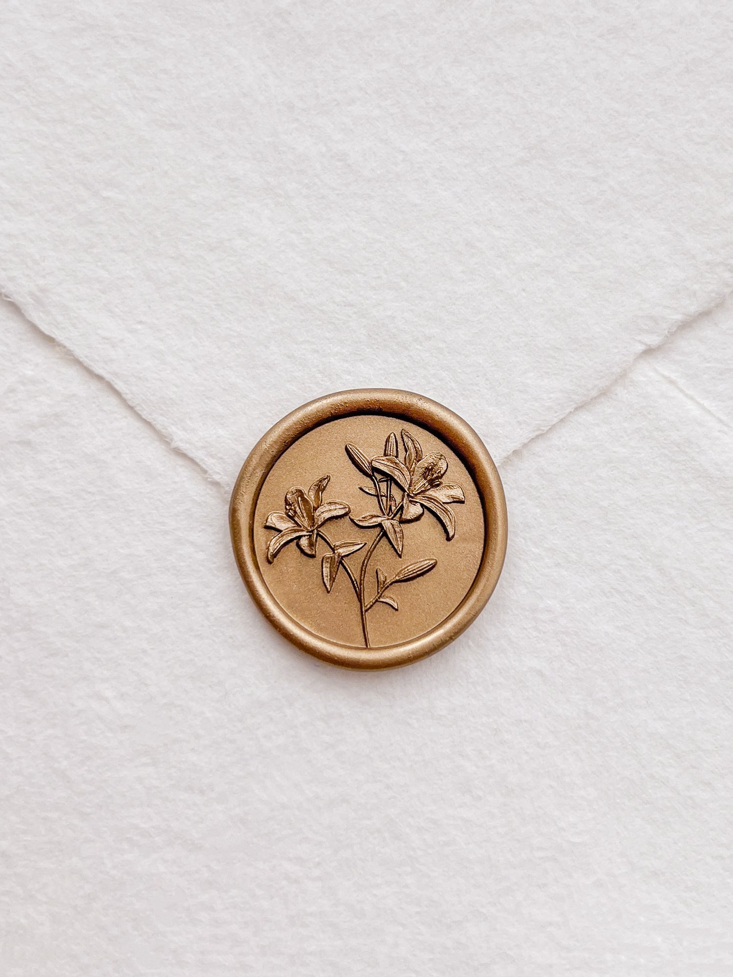 Gold lily floral seal on a white envelope