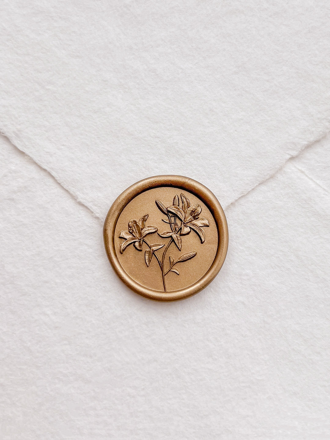 Gold 3D lily flowers wax seal on a white textured handmade paper envelope