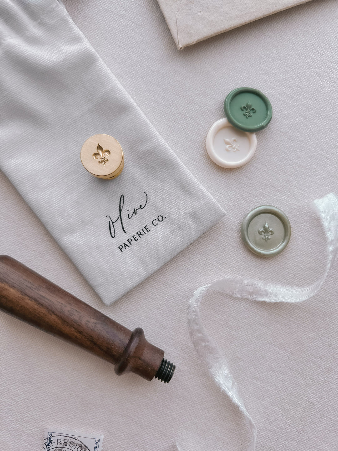 Green, off-white, and light metallic green 3D fleur de lis wax seals on a texture white background with a brass stamp head and wooden handle 