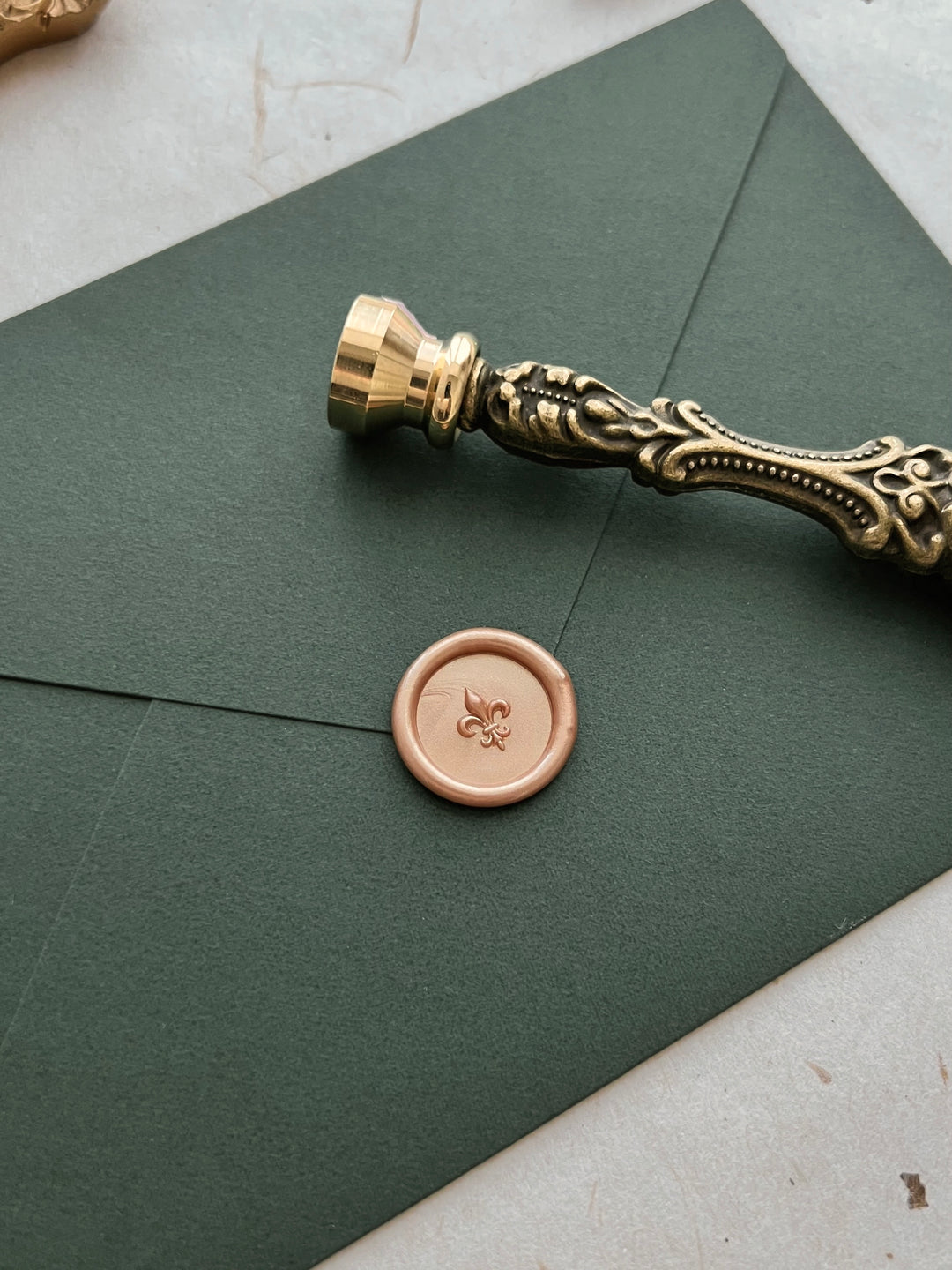 Peachy gold 3D fleur de lis mini wax seal on a dark green envelope with an ornate gold wax seal stamp