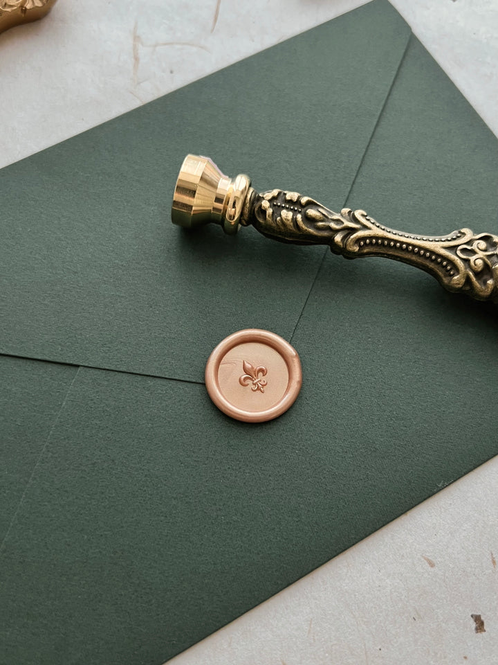 Peachy gold 3D fleur de lis mini wax seal on a dark green envelope with an ornate gold wax seal stamp