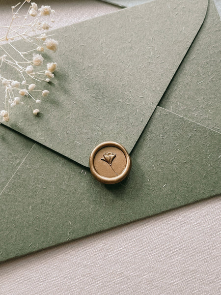 flower design gold mini wax seal on an olive green textured envelope