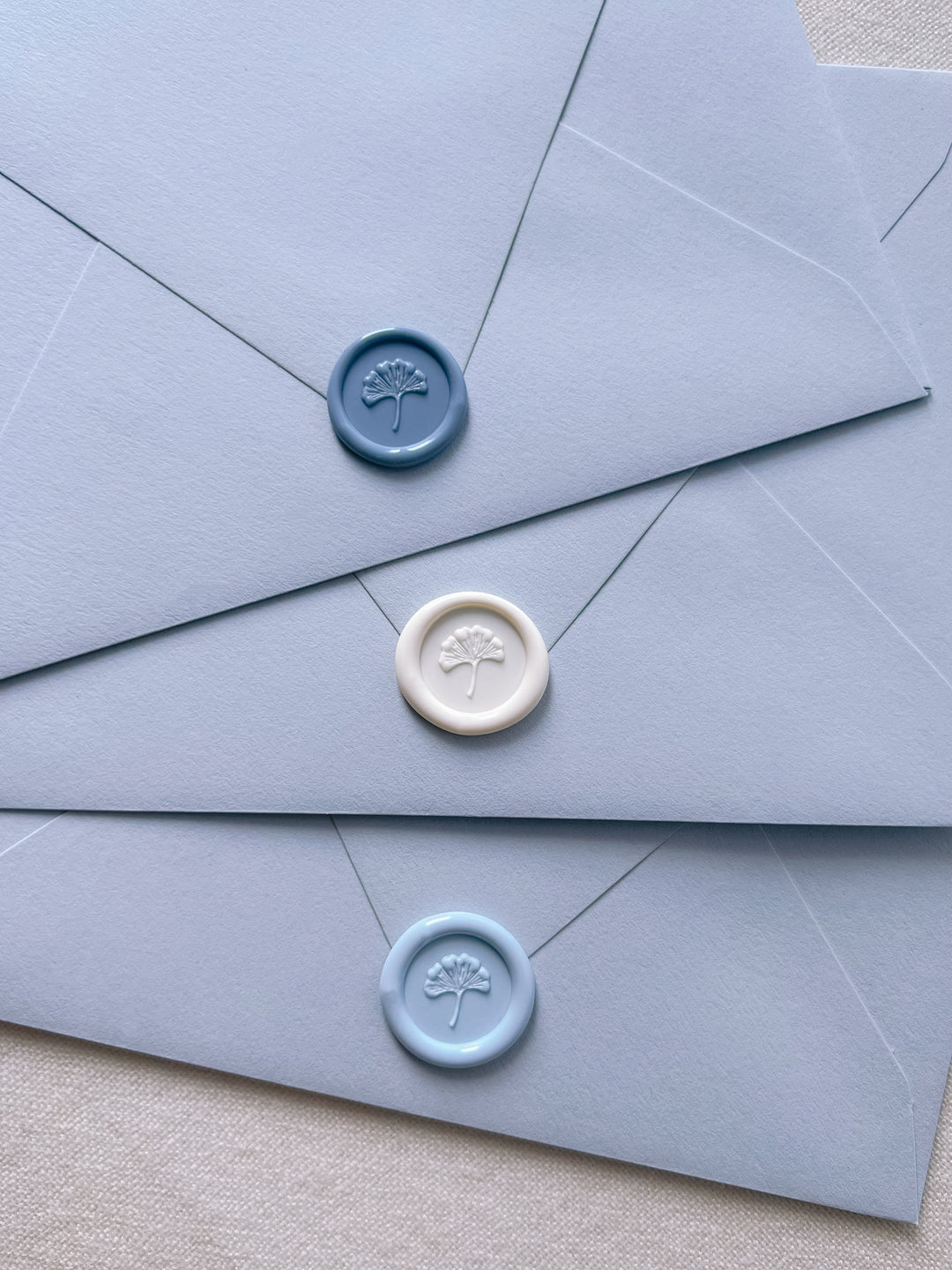 french blue, soft white, and pale blue 3D mini ginkgo wax seals on a tiered light blue wedding envelopes