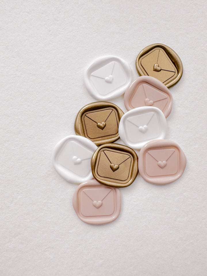 Gold, white, and light pink 3D mini heart sealed envelope love letter wax seals on a textured white background
