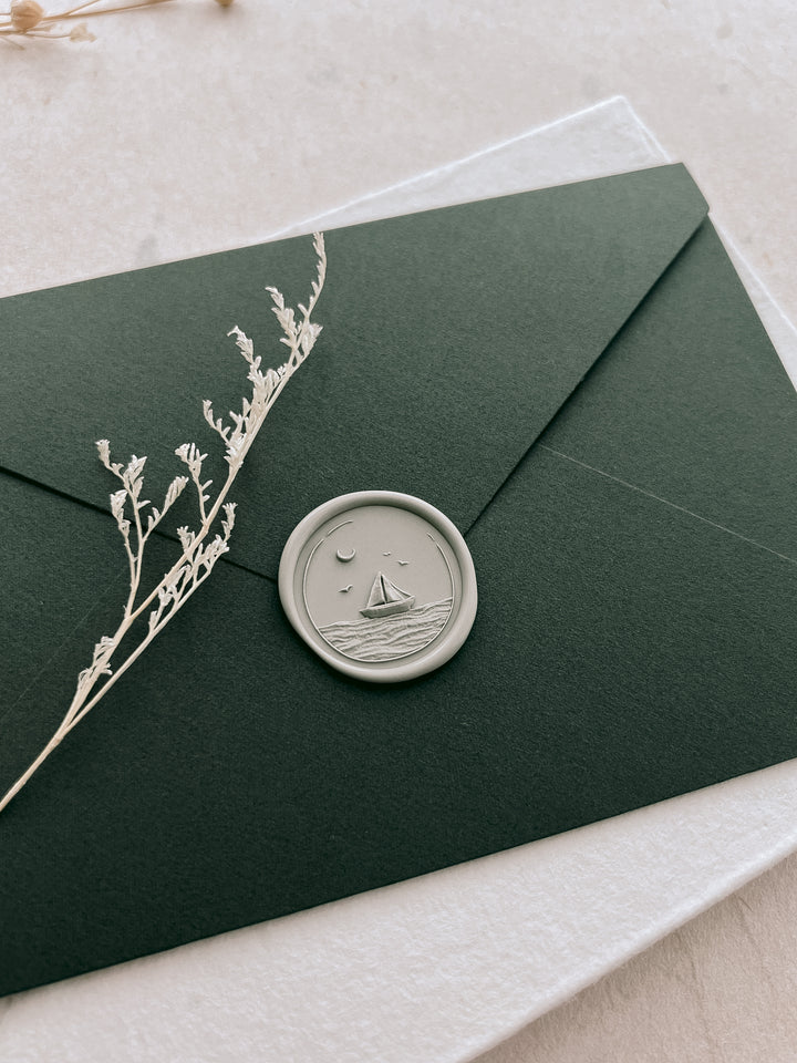 Light sage green 3D engraved sailboat and ocean waves wax seal on a dark green envelope