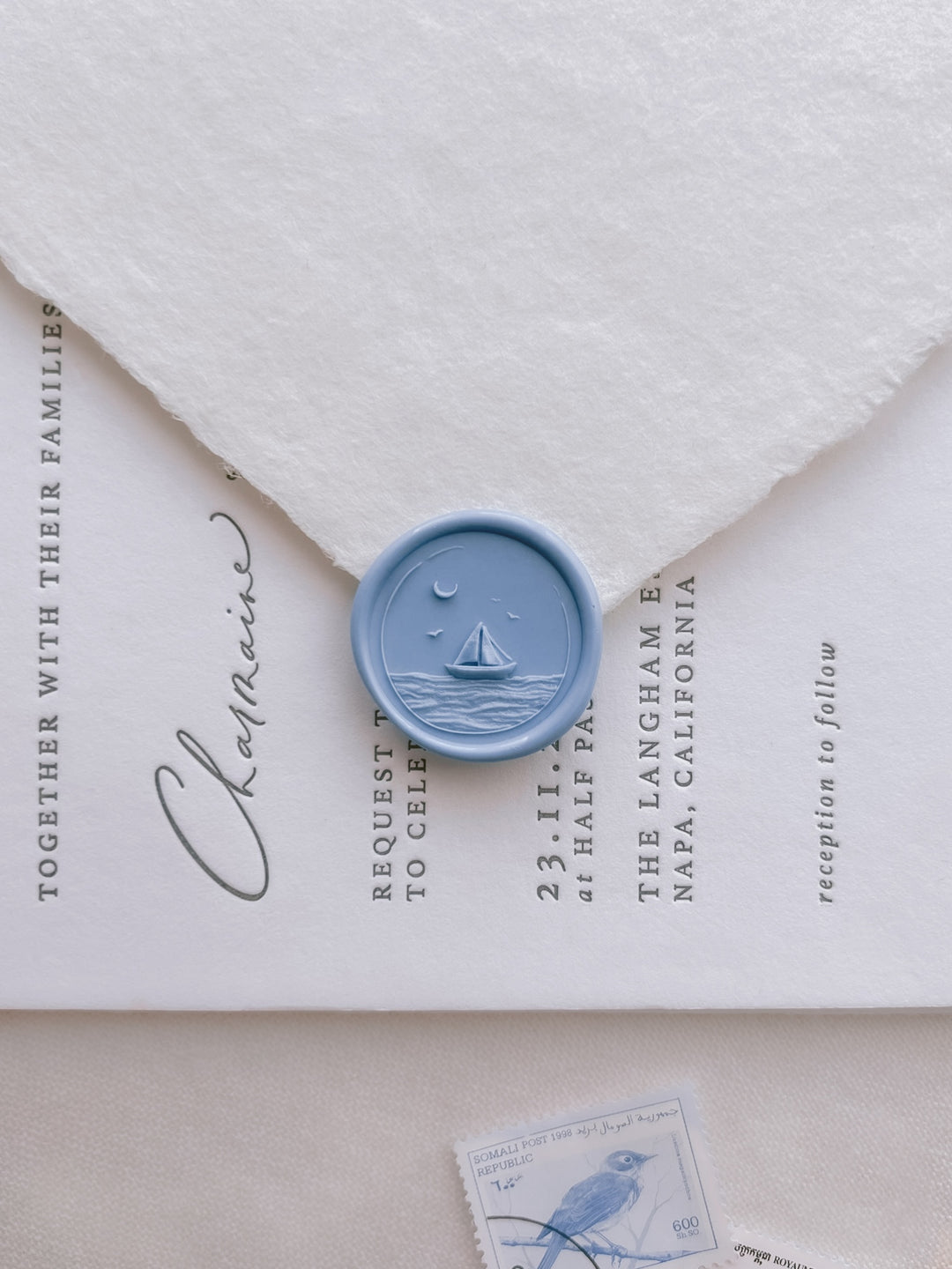Blue sailboat coastal wax seal with 3D engraving details on a white deckle-edge handmade paper envelope over a wedding invitation card