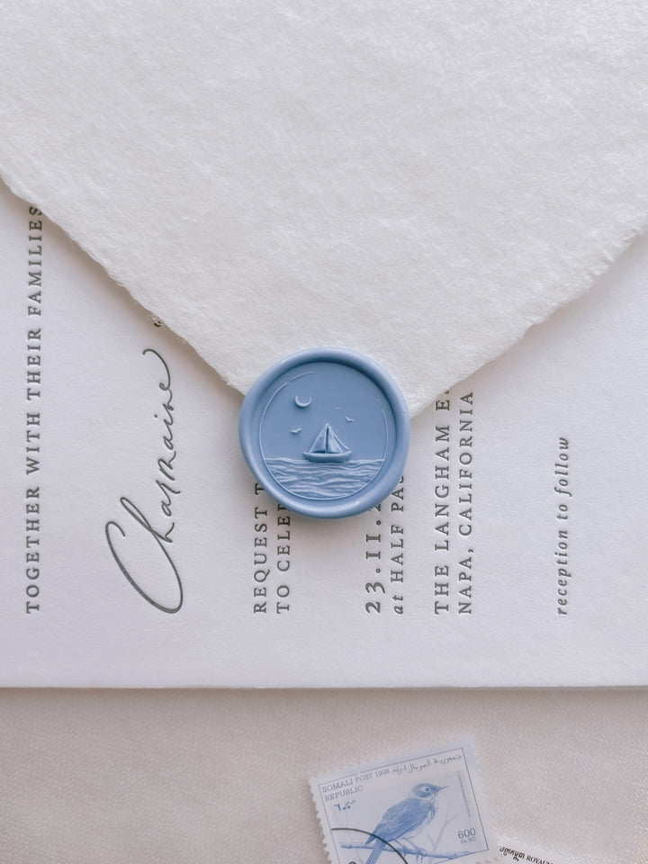Blue sailboat coastal wax seal with 3D engraving details on a white deckle-edge handmade paper envelope over a wedding invitation card
