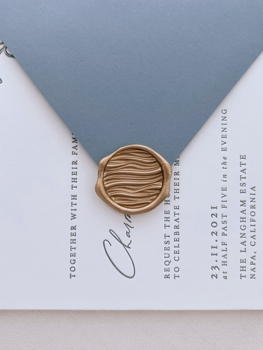 Gold 3D ocean waves wax seal on a white wedding invitation card and dusty blue envelope flap