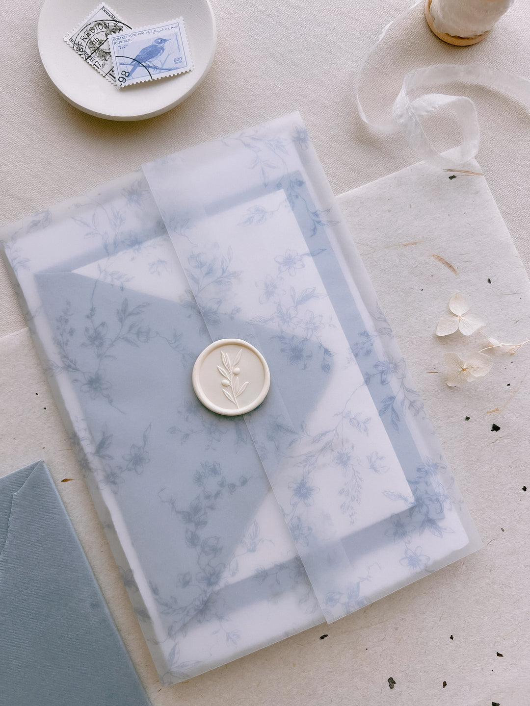 Off-white 3D olive leaf branch wax seal on a blue floral print wedding invitations vellum jacket