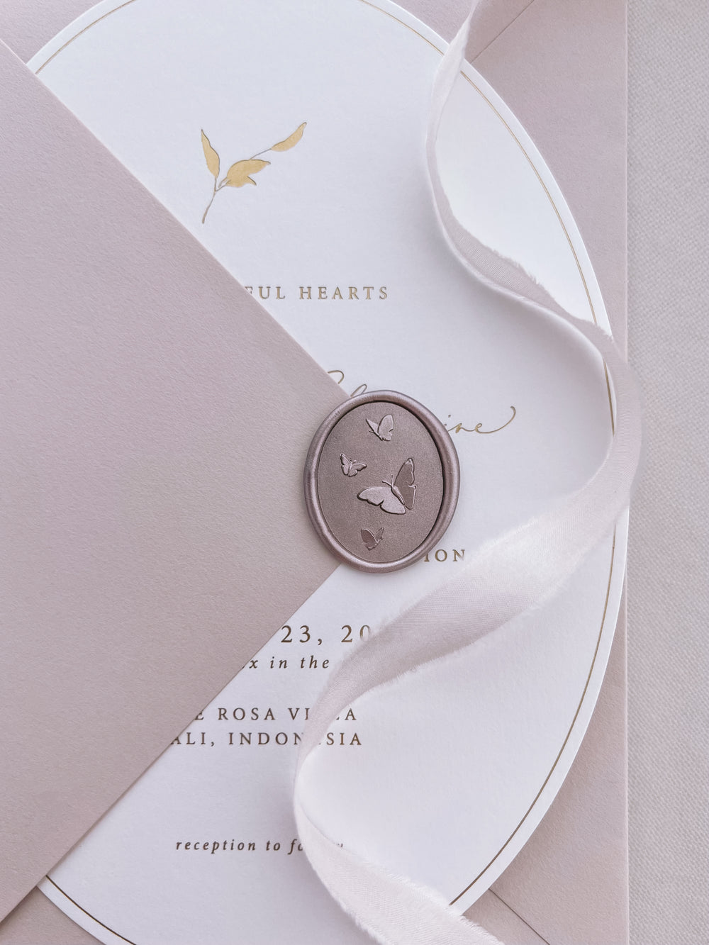 Light bronze 3D oval butterflies wax seal on a mauve envelope over an oval shaped gold foil wedding invitation card