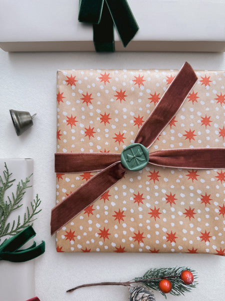 holiday-themed wax seal of a 3D ribbon bow design on festive gift wrap