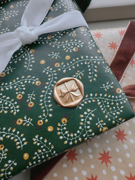 gold Christmas themed wax seal of a 3D ribbon bow design on festive gift wrap