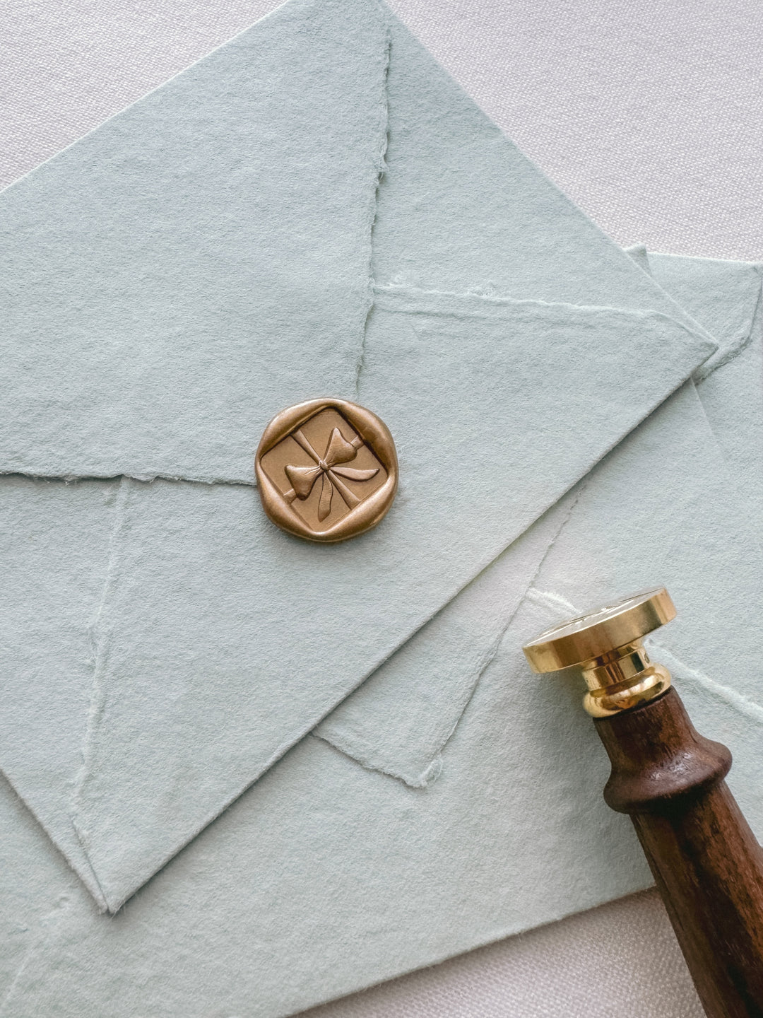 Gold square shaped gift ribbon bow wax seal on light green envelopes