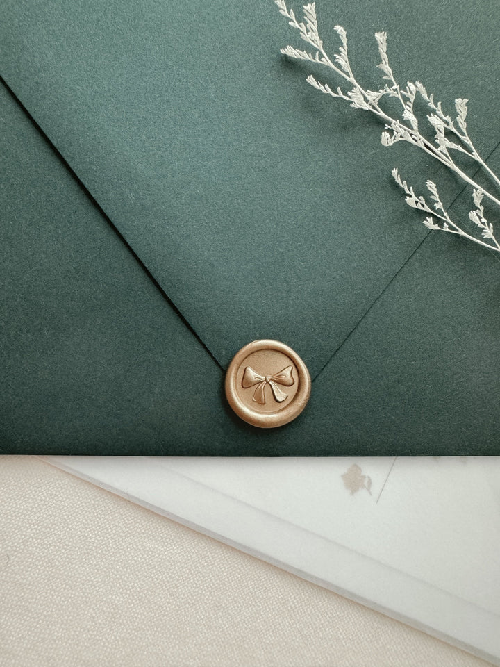 Ribbon bow mini wax seal with 3D engraving in color light gold on a dark green envelope