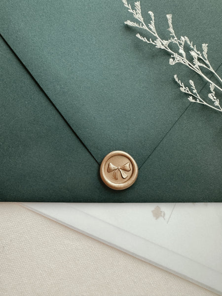 Ribbon bow mini wax seal with 3D engraving in color light gold on a dark green envelope