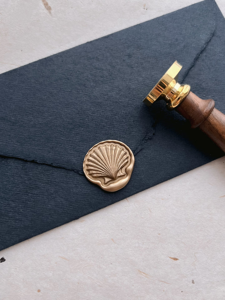 Gold 3D seashell die-cut wax seal on a black handmade paper envelope