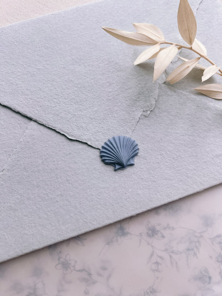 Dusty blue 3D seashell die-cut wax seal on a light blue handmade paper envelope