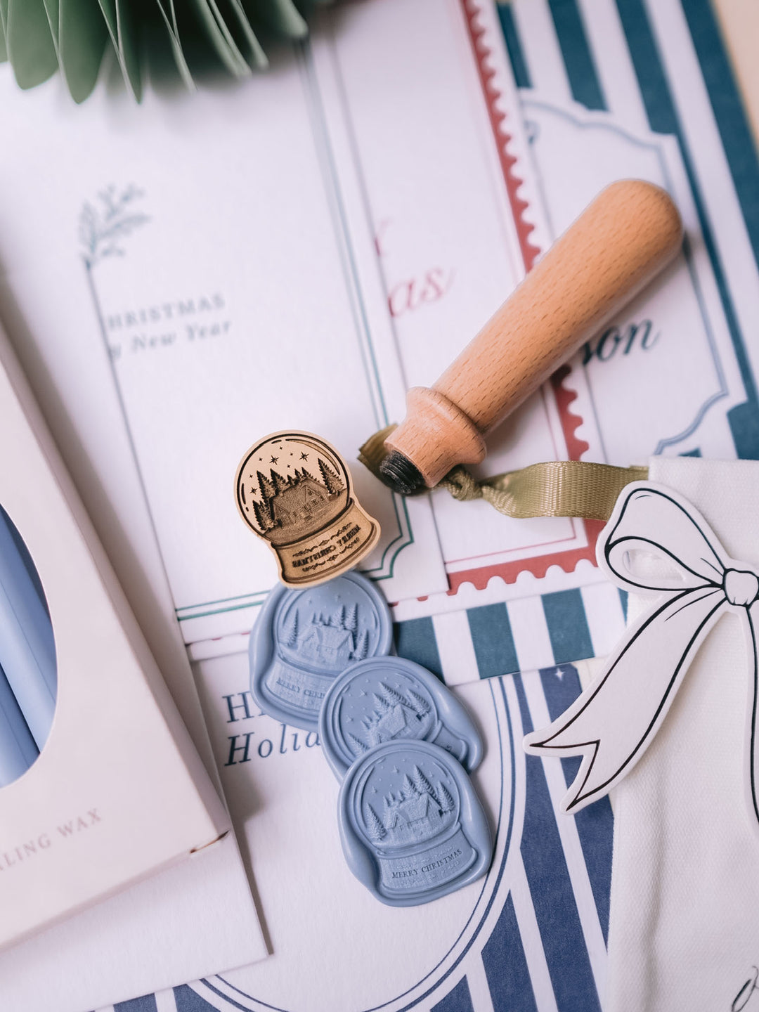 Dusty blue die-cut snow globe wax seals styled with dusty sealing wax sticks, a wooden wax stamp handle and Christmas cards