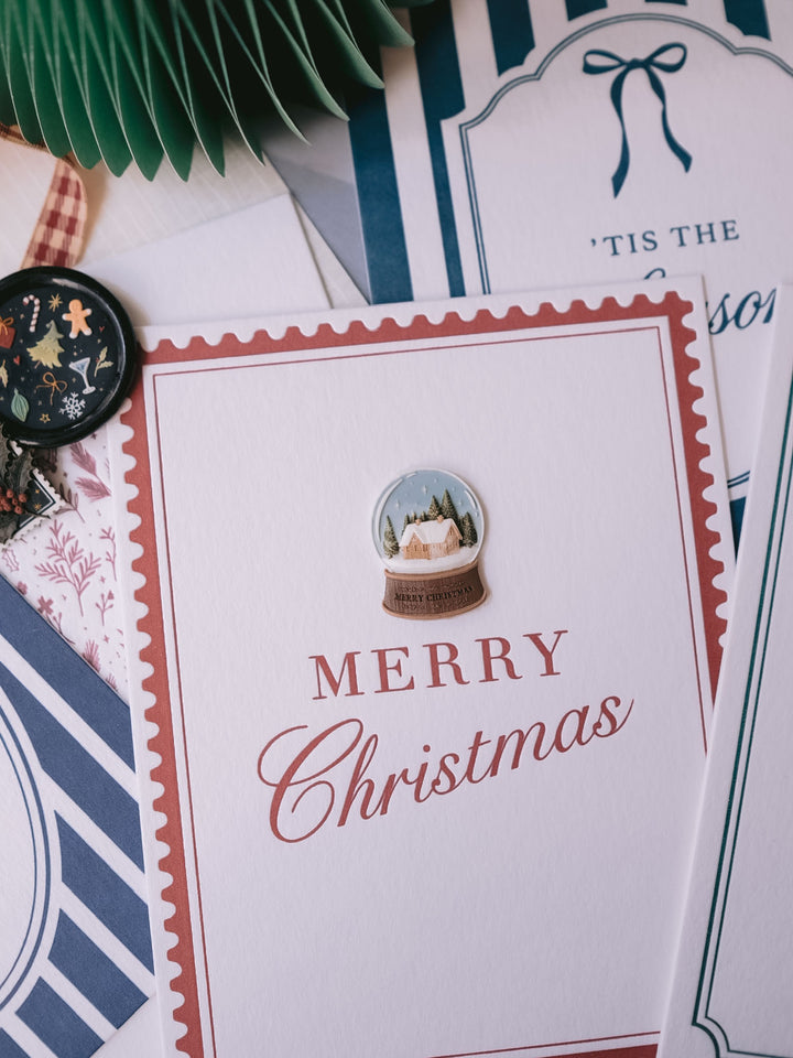 Multi-toned snow globe Merry Christmas wax seal on a holiday card printed with Merry Christmas with a red postage stamp border design 