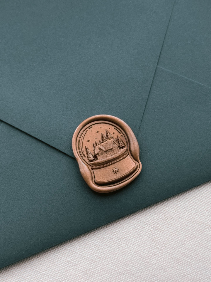 Antique bronze North Star snow globe wax seal on a dark teal envelope 