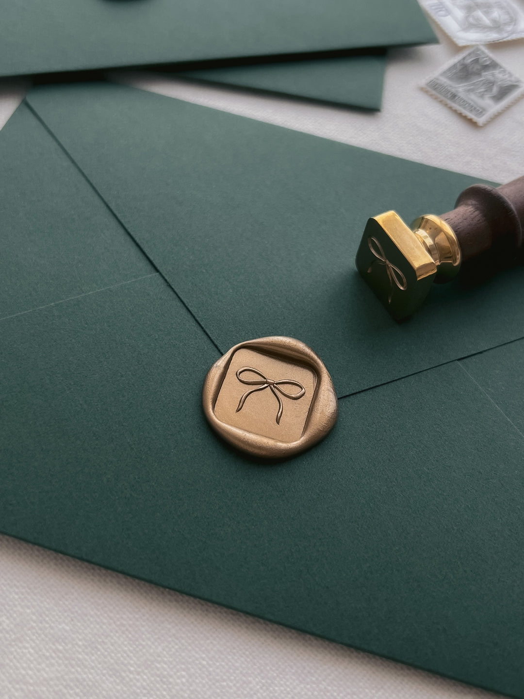 Gold 3D hand-drawn bow mini square wax seal on a dark green envelope