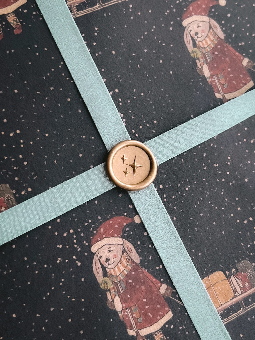 Light gold 3D stars emoji mini wax seal on a light blue ribbon on a decorative Christmas gift wrap