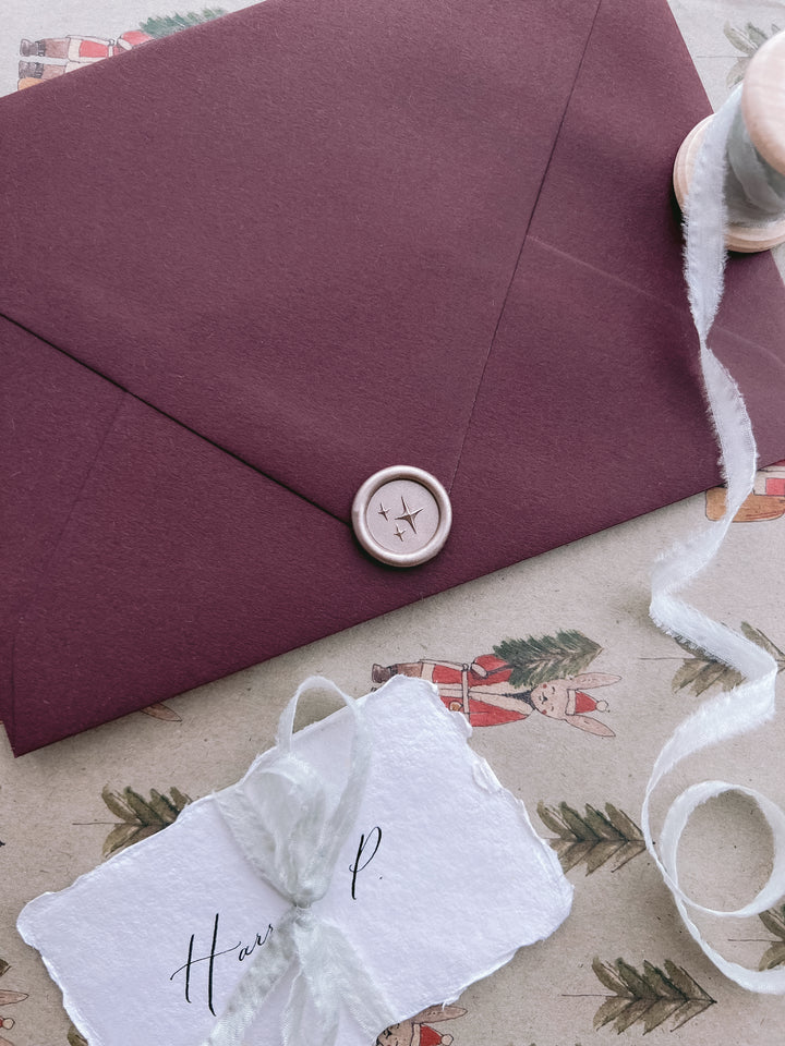 Light bronze 3D stars emoji mini wax seal on a deep burgundy envelope, styled with white silk ribbon and white place cards