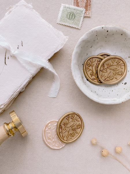Oval floral pattern wax seals in colors gold and nude pearl styled with handmade paper place cards, ceremic dish and postage stamps