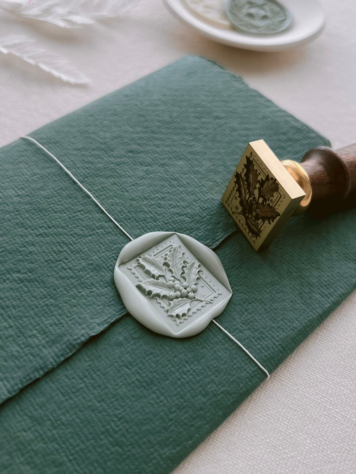 a green paper with a white wax seal and a gold stamp placed on top of it.