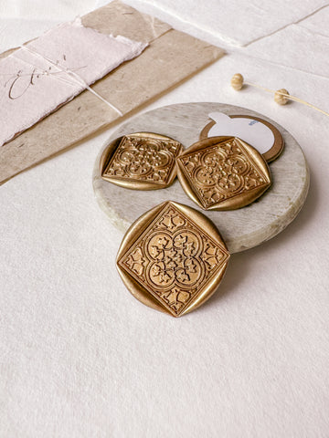 Moroccan tile quatrefoil pattern gold wax seals styled with a small gray stone dish, handmade paper and a dried floral branch