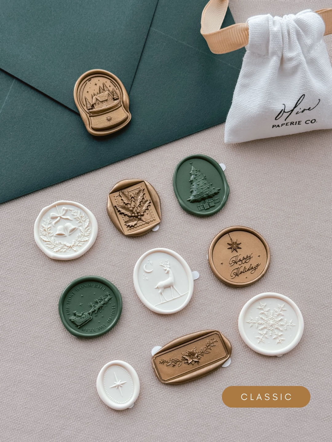 Assorted Christmas wax seal stickers in gold, dark green and ivory — ten festive designs laid out beside a dark green envelope and linen pouch.