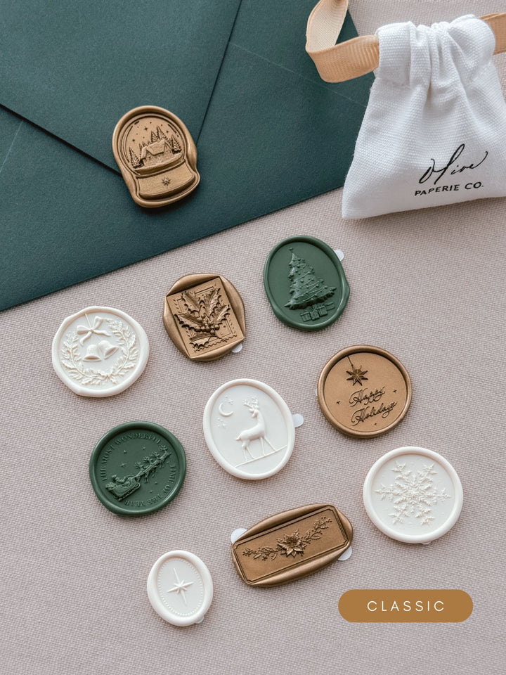 Assorted Christmas wax seal stickers in gold, dark green and ivory — ten festive designs laid out beside a dark green envelope and linen pouch.