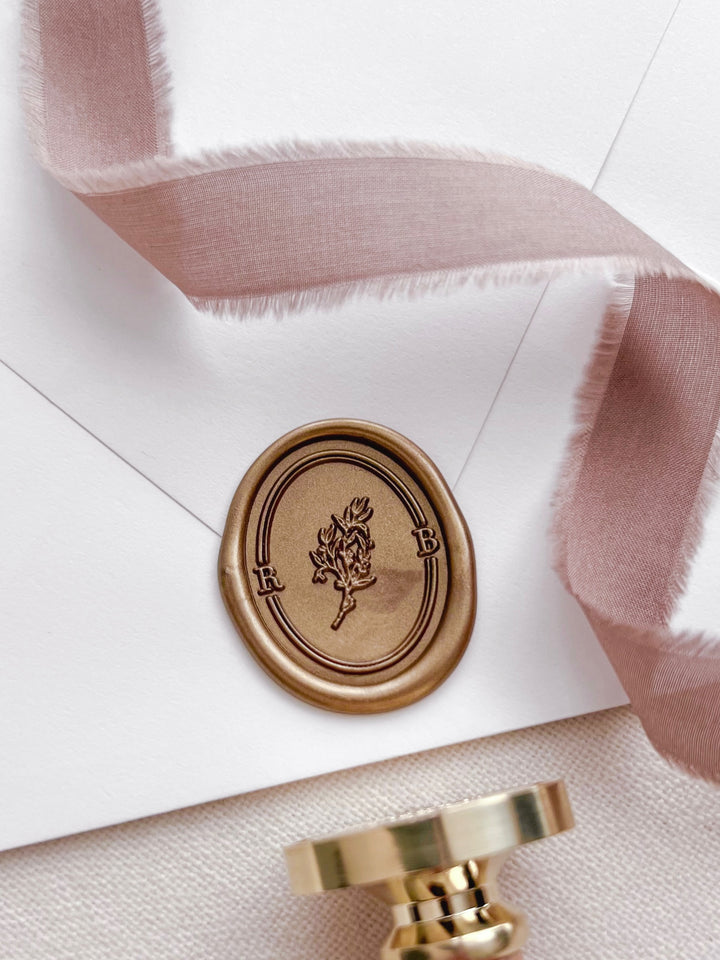 Personalized initials gold botanical monogram oval wax seal featuring a custom monogram with oval line border on a white envelope with a wax stamp head on a light beige background