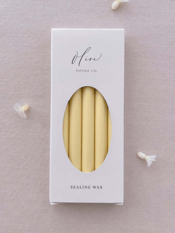 Butter yellow sealing wax sticks in Olive Paperie Co. branded packaging, displayed on a soft linen backdrop with dried flower details.