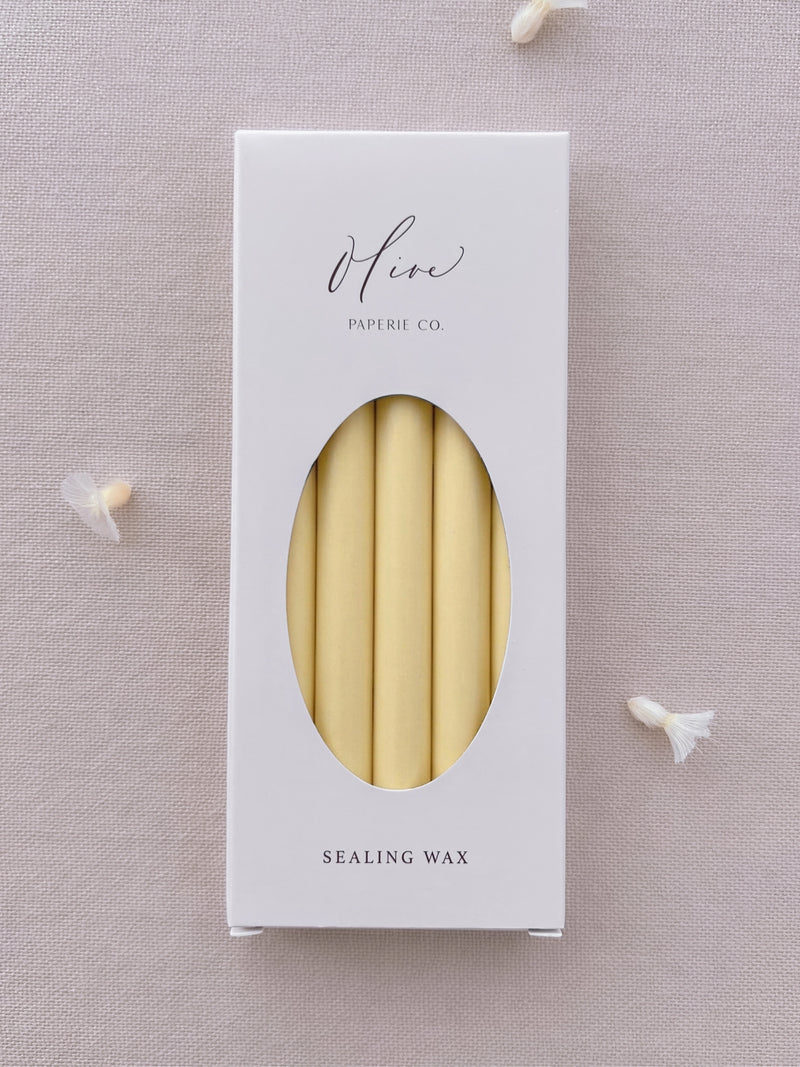 Butter yellow sealing wax sticks in Olive Paperie Co. branded packaging, displayed on a soft linen backdrop with dried flower details.