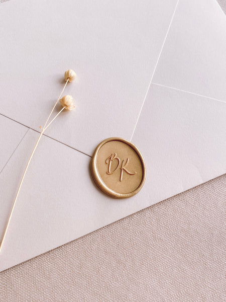 Calligraphy monogram oval custom wax seal in light gold on white paper envelope styled with dried flowers
