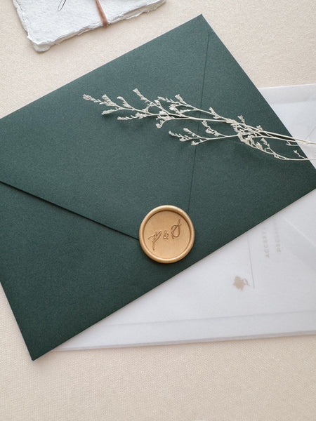 Calligraphy script monogram light gold wax seal on a dark green envelope