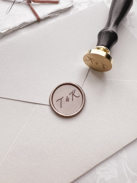 Calligraphy monogram wax seal in a light bronze color on a beige envelope next to a wax seal stamp