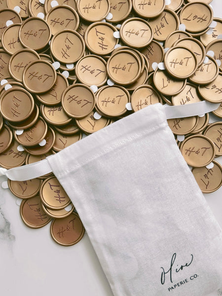 Calligraphy script monogram gold wax seals with adhesive backings placed next to a white linen pouch