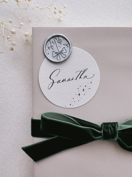 festive silver wax seal with ornament and ribbon bow design attached on a wrapped Christmas gift with a name tag