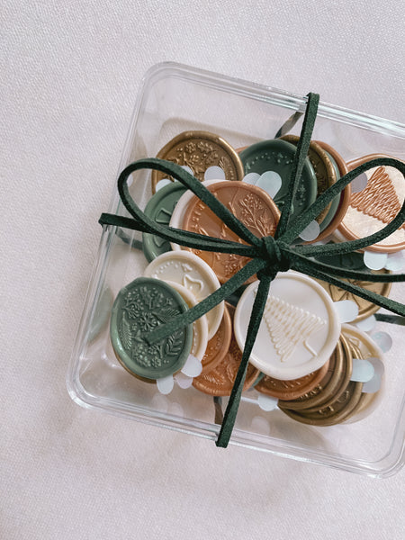 A box of assorted designs and colors in antique white, sage, light gold and gold Christmas wax seal stickers wrapped with Christmas dark green suede ribbon 