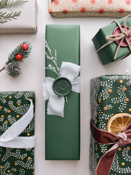 Dark green festive ornaments wax seal decorated on a wrapped Christmas gift with white silk ribbon
