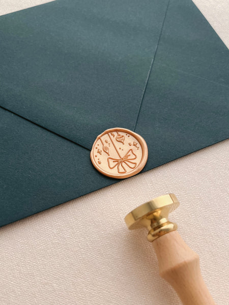 Holiday ornament wax seal in peachy gold color on dark green envelope