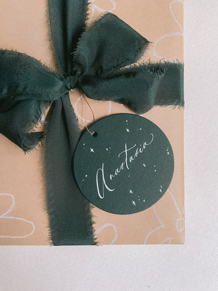 Wrapped gift with Christmas dark green silk ribbon box and Christmas round name tag in deep green close up view